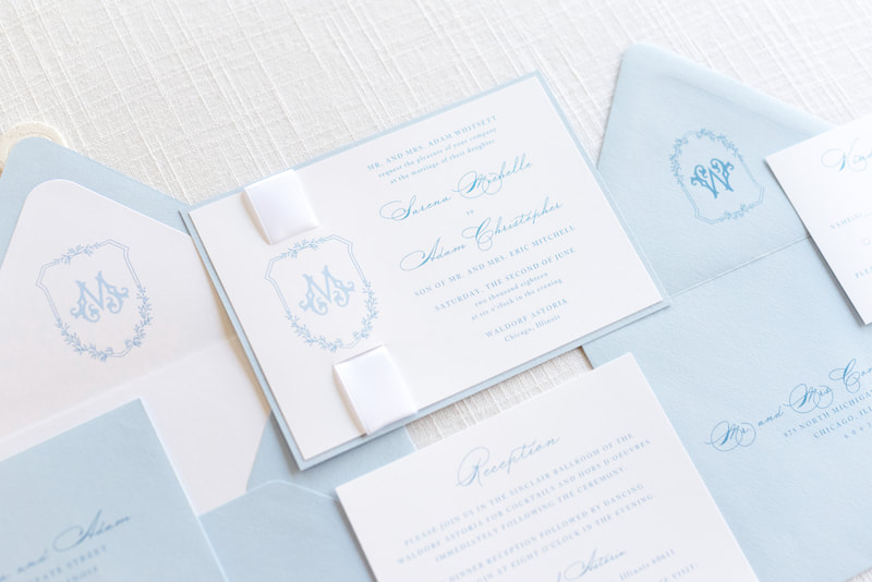 elegant and formal monogram crest wedding invitation with satin ribbon and wax seal embellishment in white, pale blue, light dusty blue