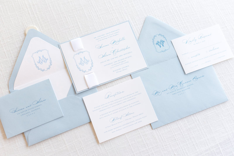 elegant and formal monogram crest wedding invitation with satin ribbon and wax seal embellishment in white, pale blue, light dusty blue